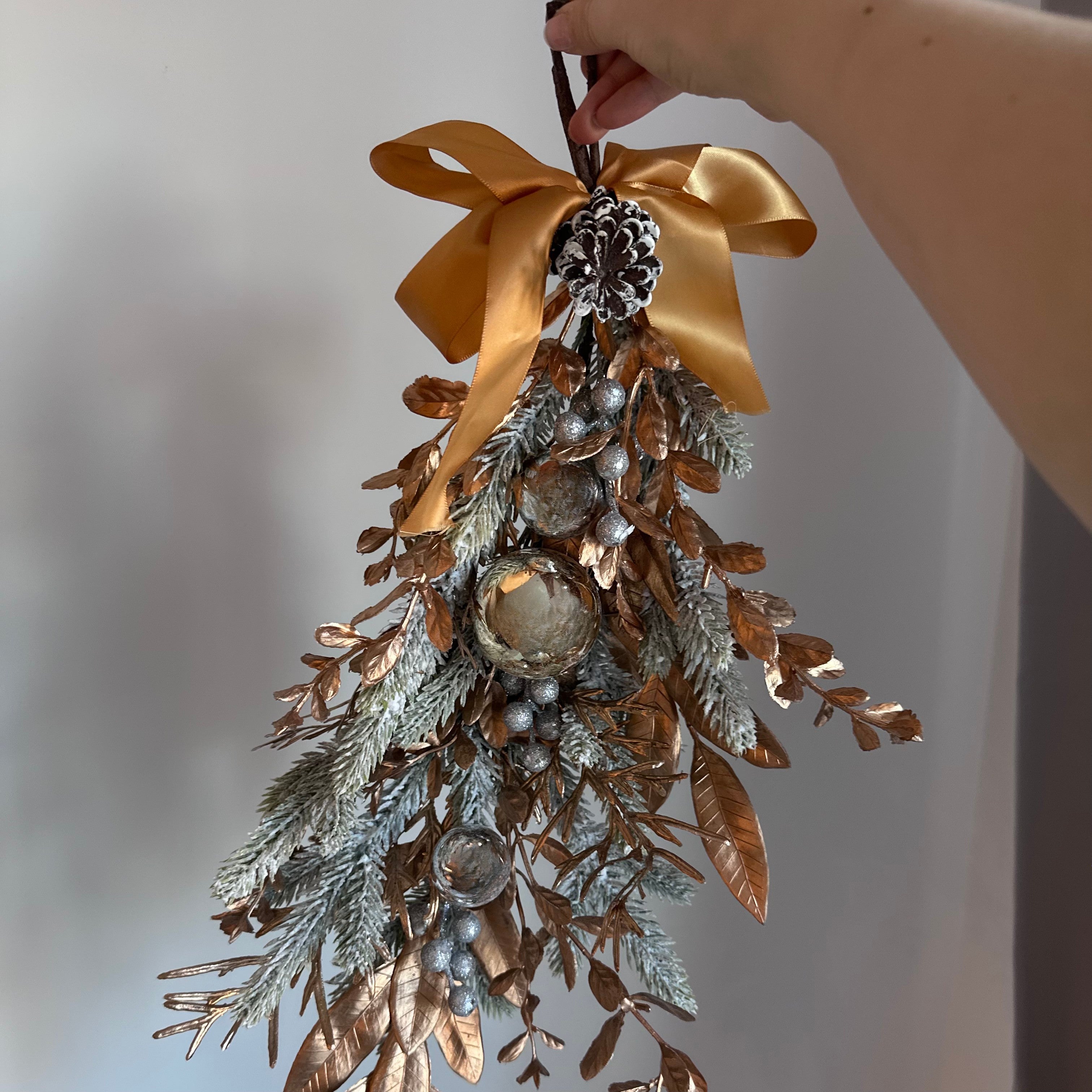 Decorative hanging with gold bow, pinecones, and branches on a neutral background