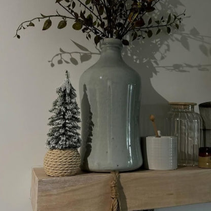 Decorative shelf with a large ceramic bottle, small Christmas tree, and various items against a light wall.