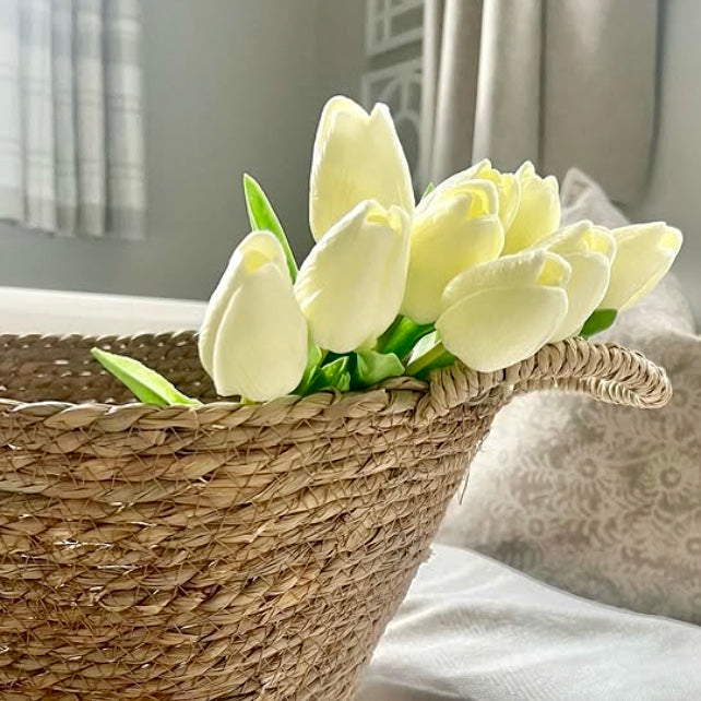 White tulips in a woven basket on a light surface with a neutral background