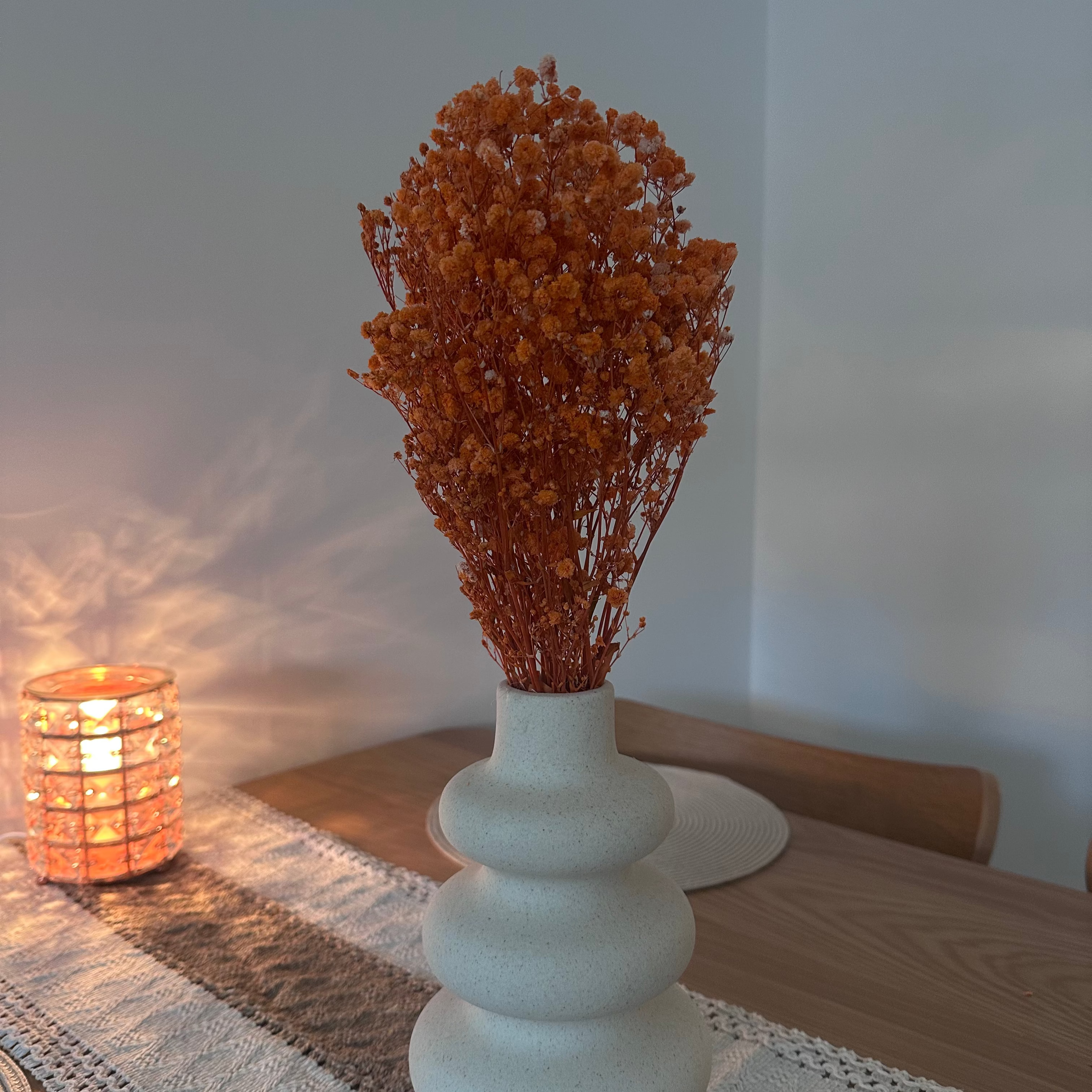 White vase with dried gypsophila flowers on a table next to a lit candle