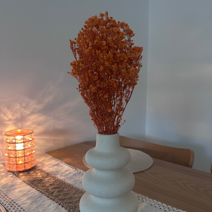 White vase with dried gypsophila flowers on a table next to a lit candle