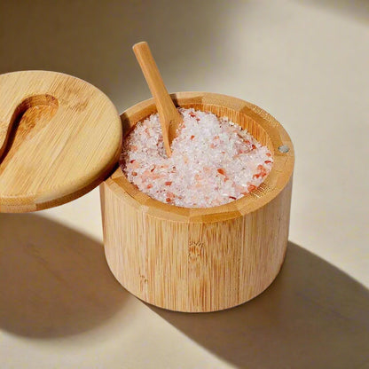 Bamboo container with swing lid and matching wooden spoon, filled with pink Himalayan salt on a white background