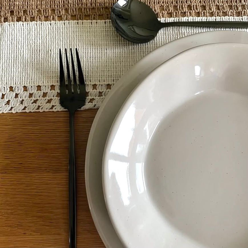 White plate with black fork and spoon on a textured placemat