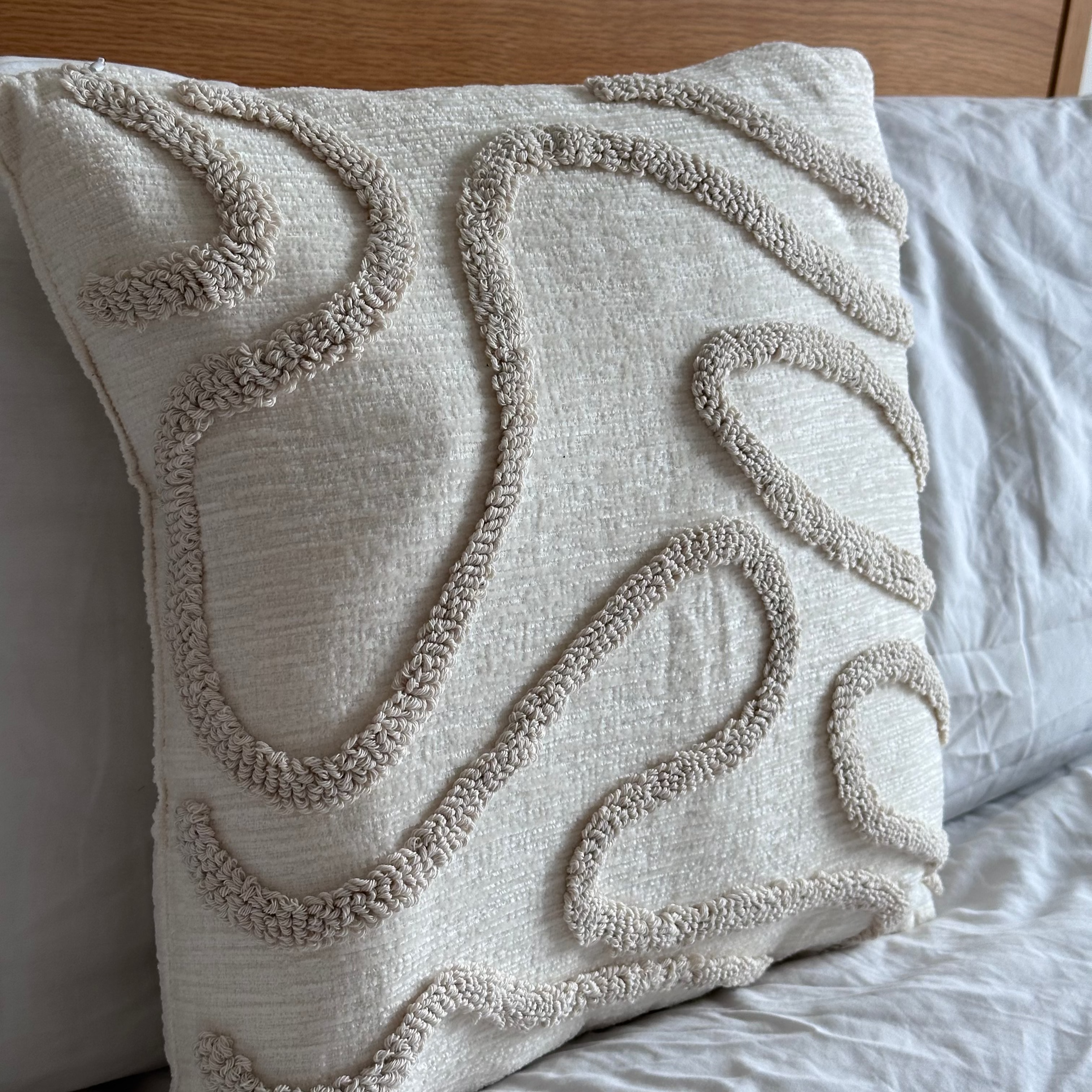 Textured pillow on a bed with a wooden headboard beige