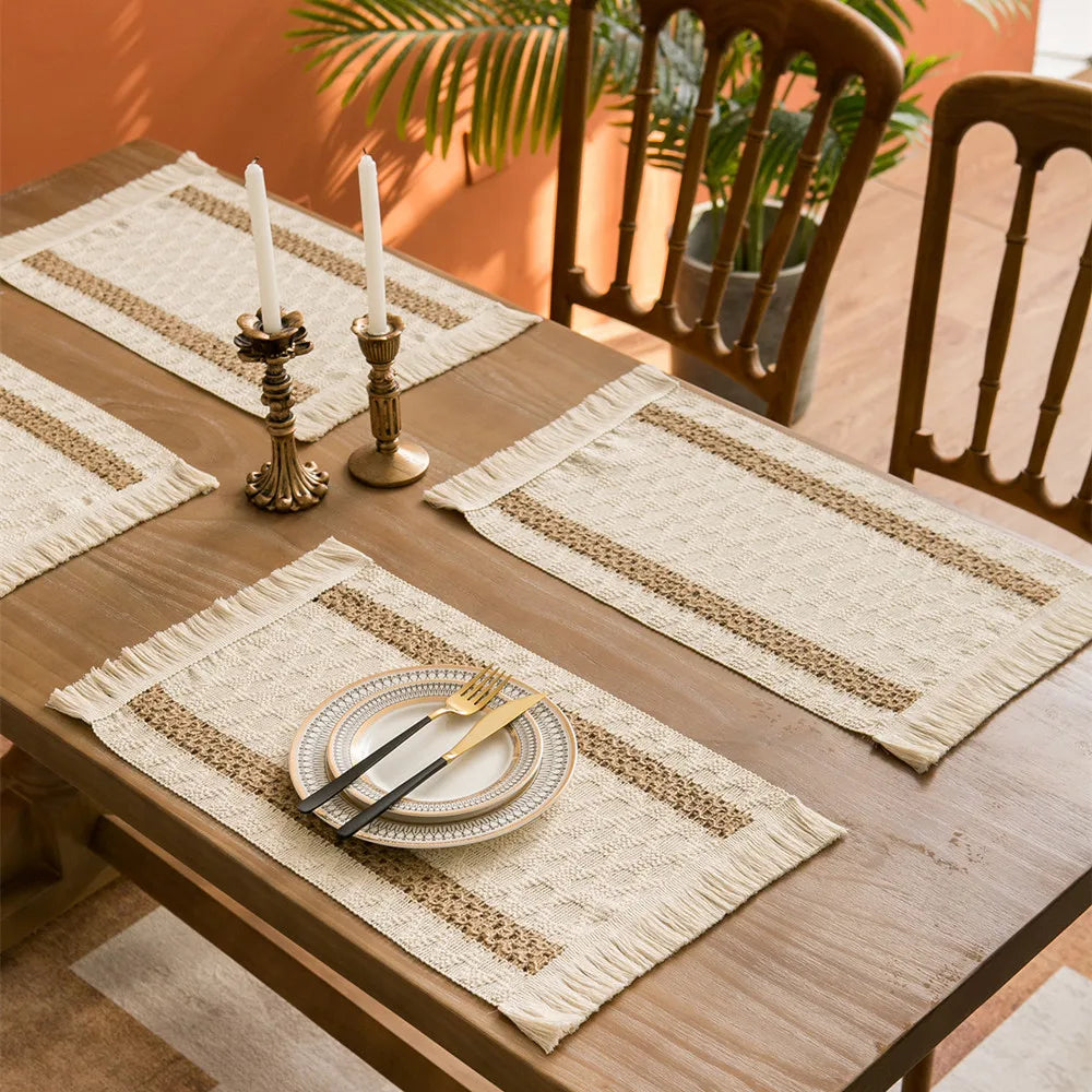 Dining table set with boho farmhouse placemats, candles, and cutlery on a wooden table.