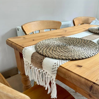 Wooden dining table with a woven placemat and boho table runner, surrounded by chairs.