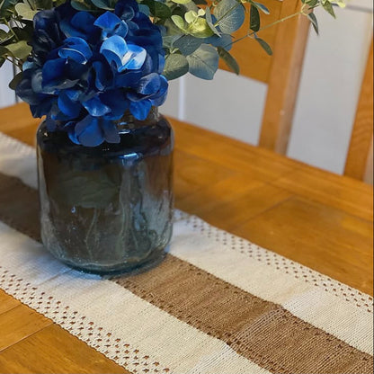 Blue flowers in a dark vase on a wooden table with boho table runner featured. 