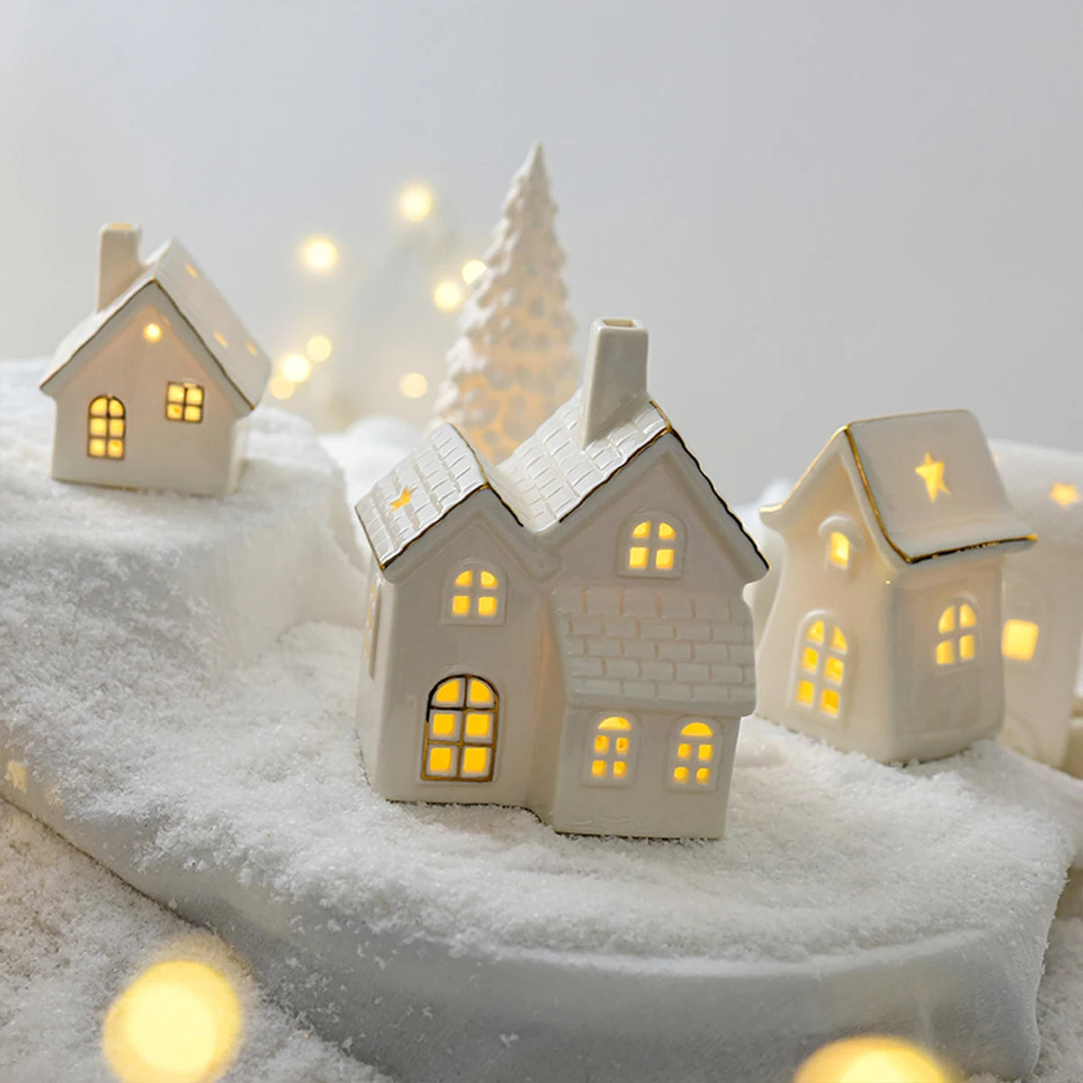 A set of ceramic Christmas houses with lights, designed to create a mini Christmas village scene, placed on a surface with snow and decorative lights.