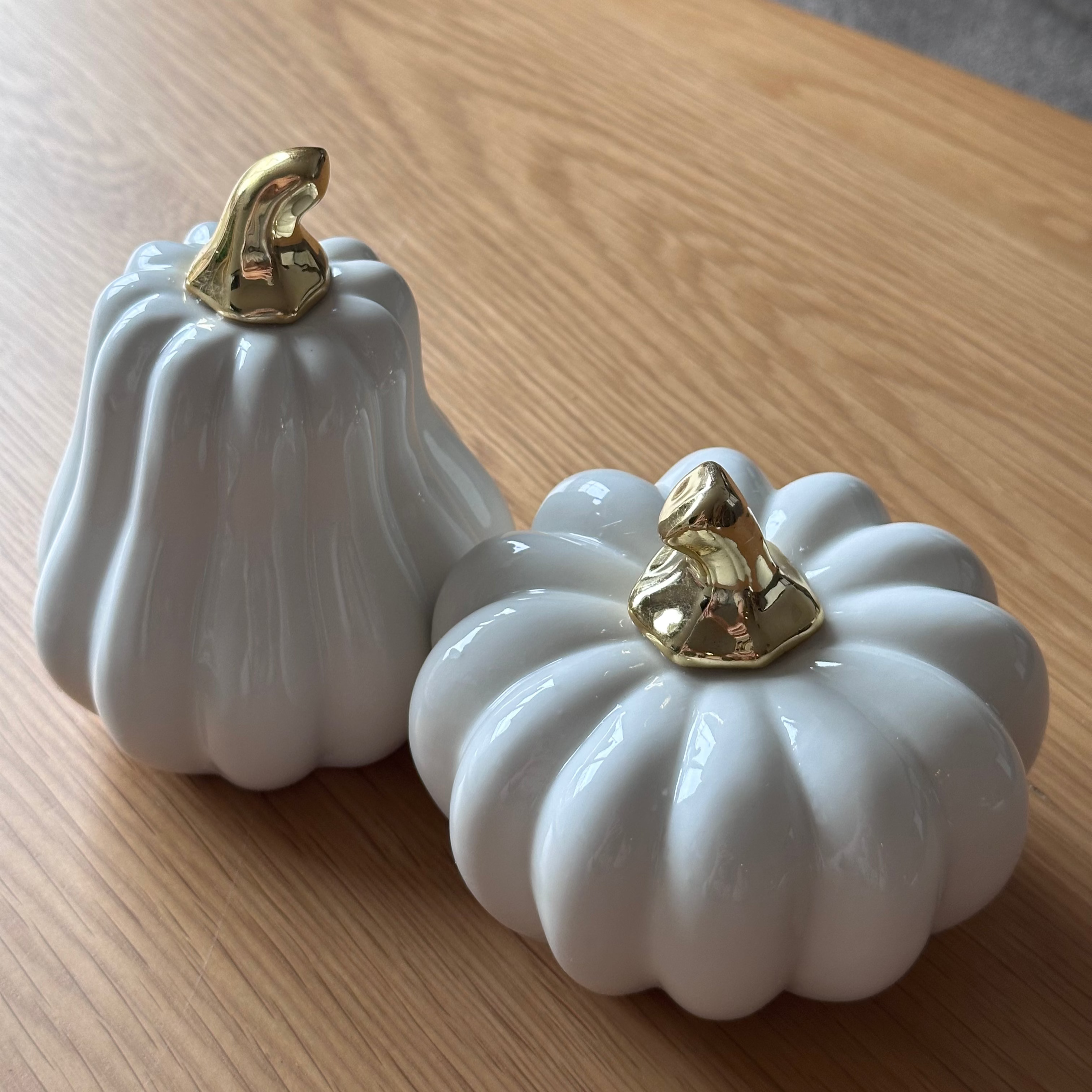 Two white ceramic pumpkins with gold accents on a wooden surface.