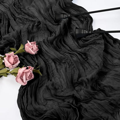 A close-up of a pink cheesecloth rustic table runner draped on a white surface, with three pink roses laid on the cloth.