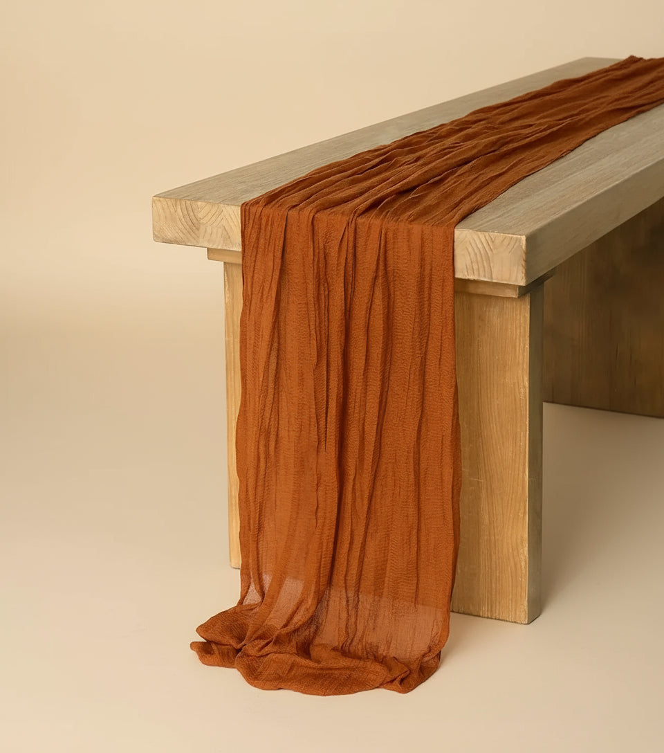A brown cheesecloth table runner with a rustic design, laid out on a wooden dining table. 