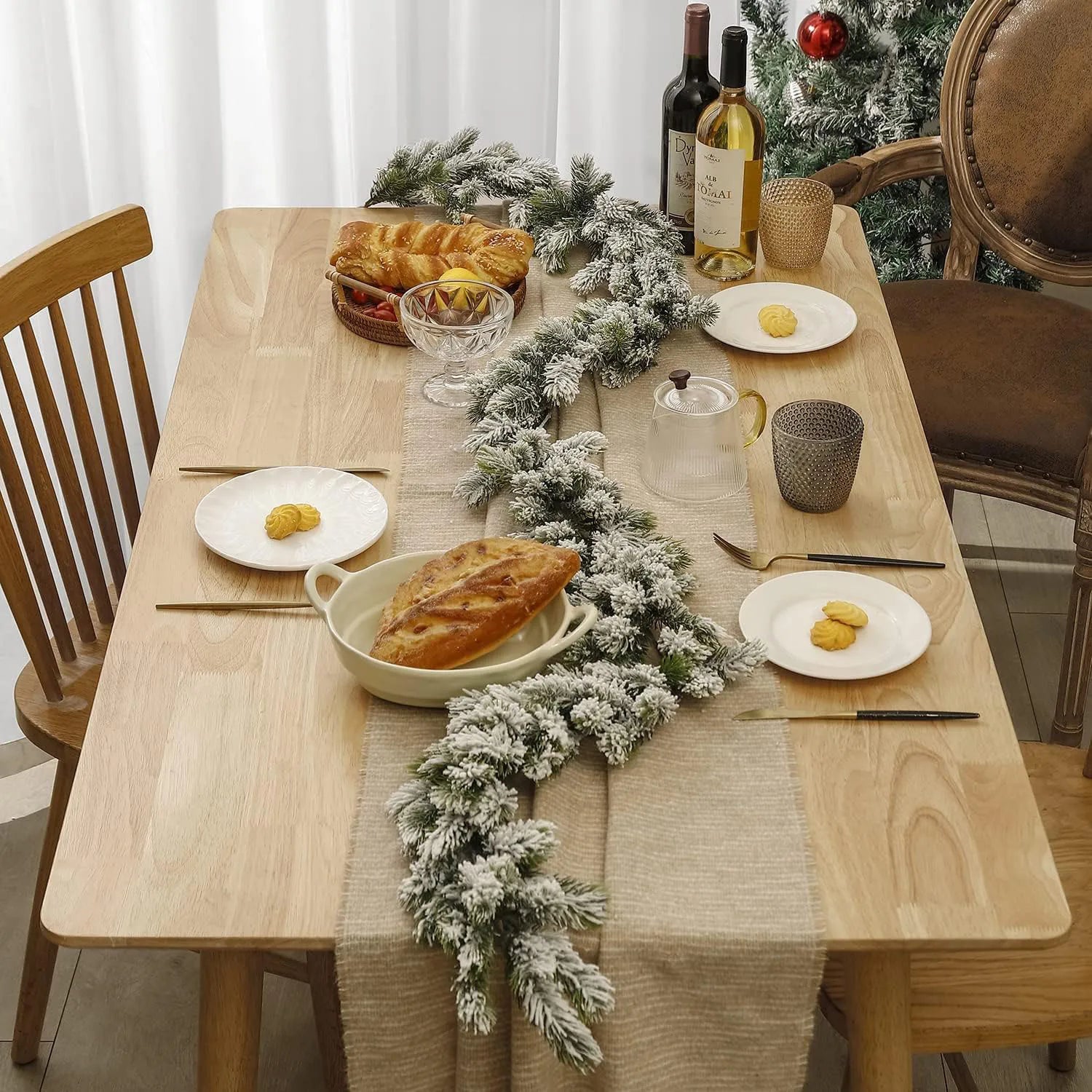 A 6.2ft snowy Christmas garland with frosted pine needles displayed on a wooden dining table with plates and cutlery set. 