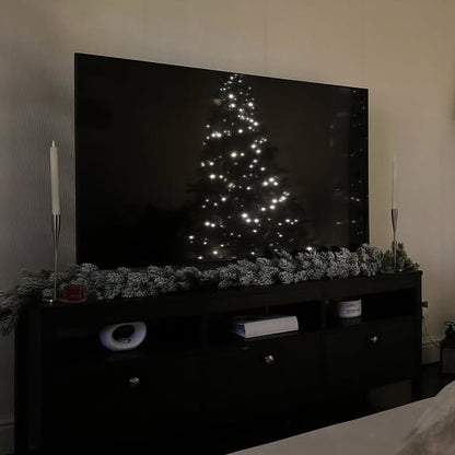 TV displaying a Christmas tree with lights on a decorative shelf.