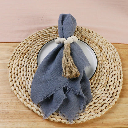 A folded cotton napkin in blue color is placed on a round woven mat, with a decorative touch added by a string tied in a bow on top of the napkin.