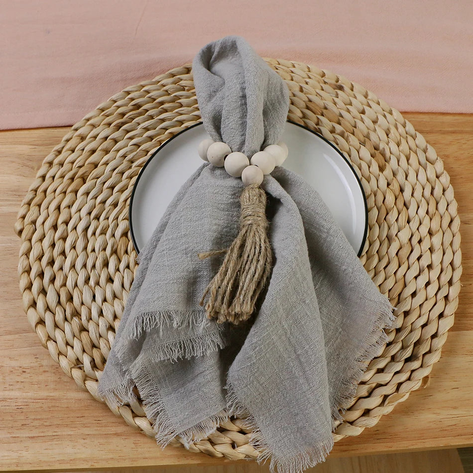A grey cotton napkin is draped over a round wicker plate, with a decorative tassel-like string attached to the napkin.