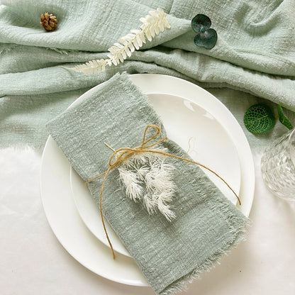 A light green cotton napkin is draped over a white ceramic plate, with a decorative tassel-like string attached to the napkin.