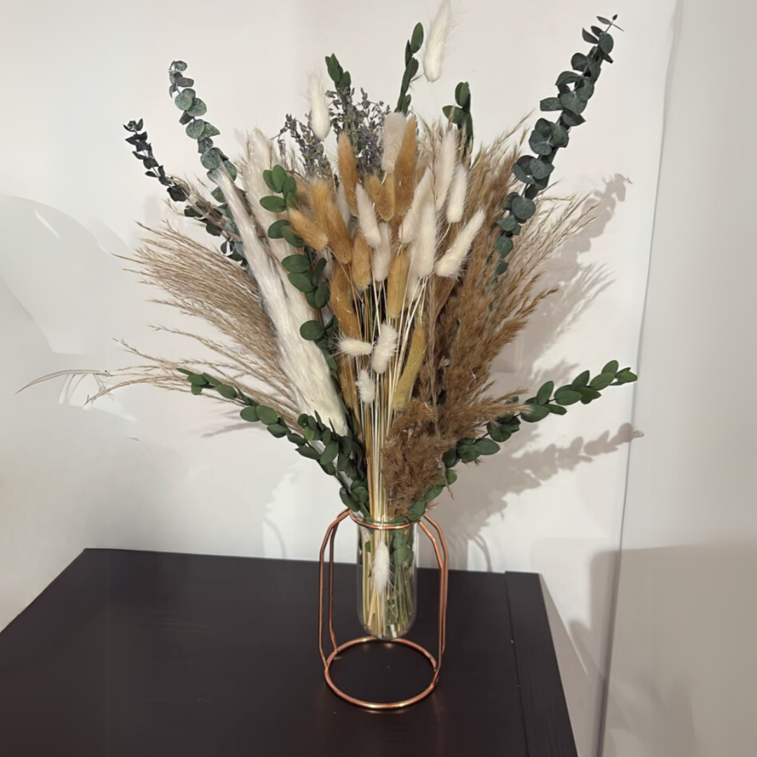 Bouquet of dried pampas in a clear vase with a bronze stand on a black surface.