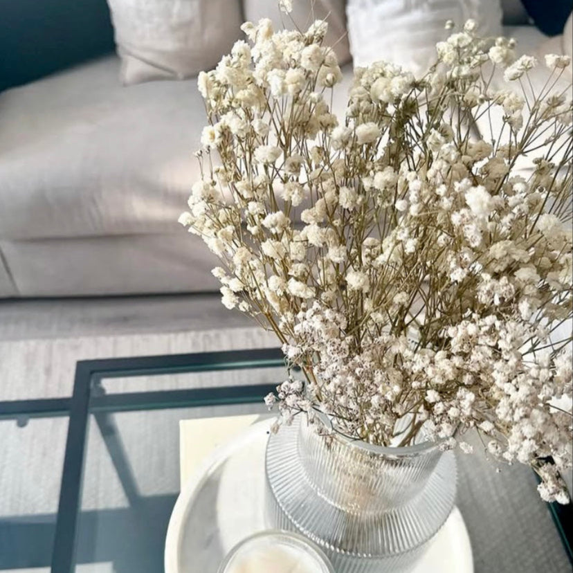 Bouquet of white dried gypsophila flowers in a vase on a coffee table with a sofa in the background