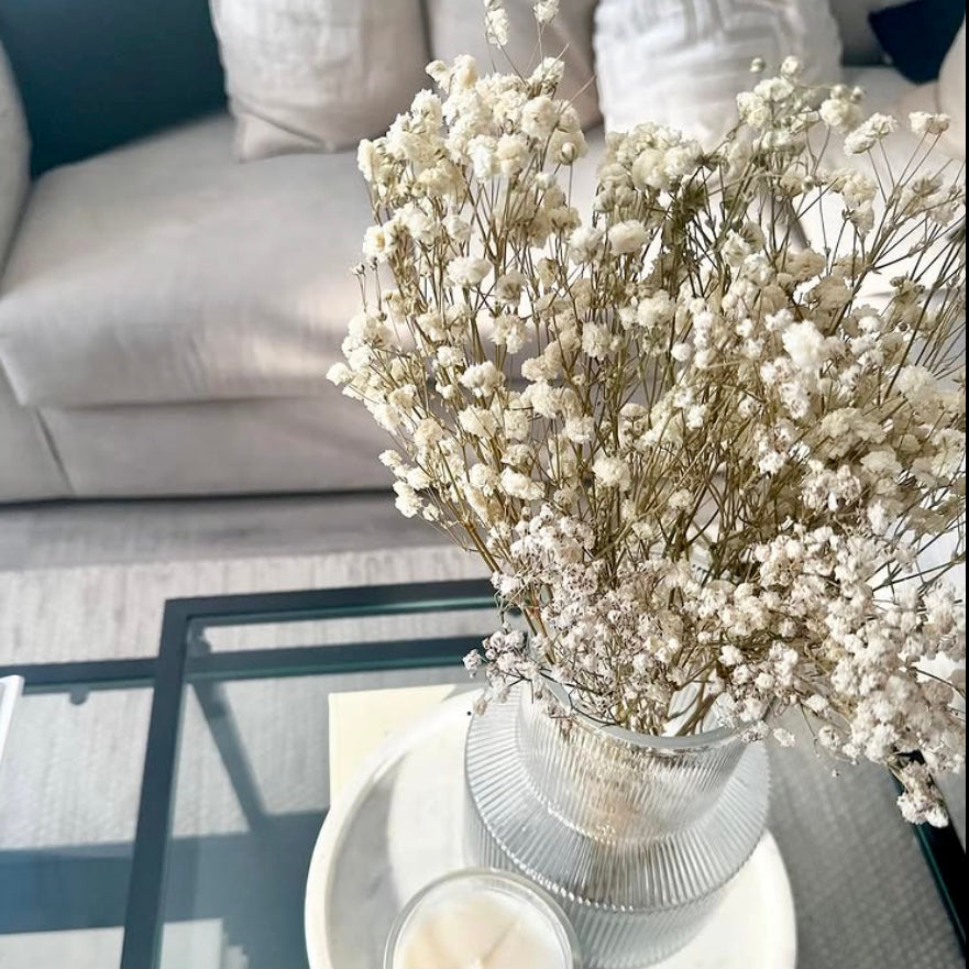 Bouquet of white dried gypsophila flowers in a vase on a coffee table with a sofa in the background