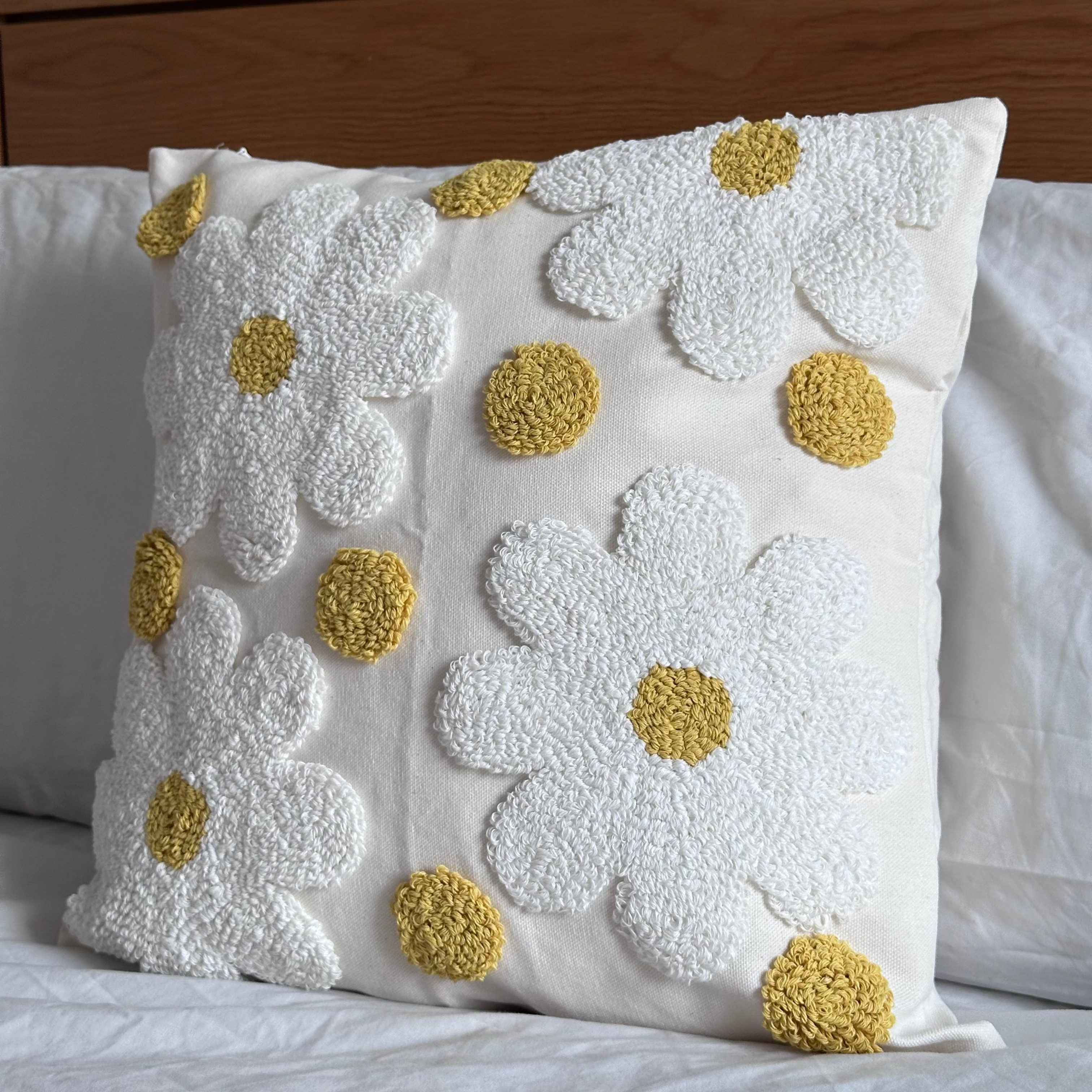 Decorative cushion with white floral patterns and yellow centers on a bed.