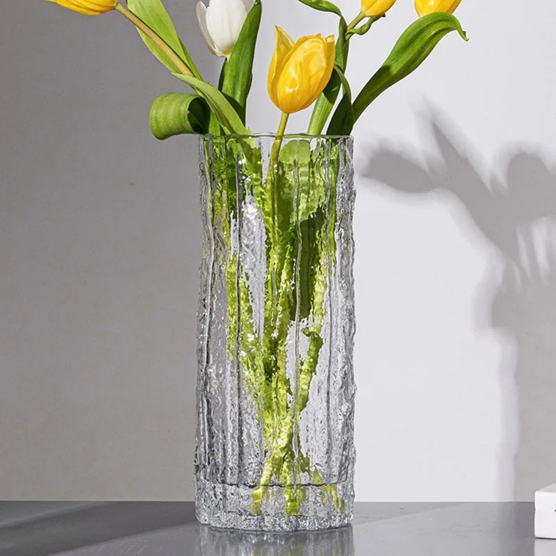 Clear glass vase with ripple effect and yellow tulips on a grey surface