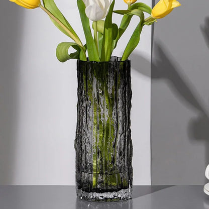Decorative smoke grey, glass vase with textured design holding yellow and white tulips on a neutral background