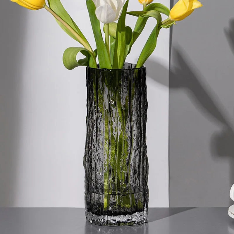 Decorative smoke grey, glass vase with textured design holding yellow and white tulips on a neutral background