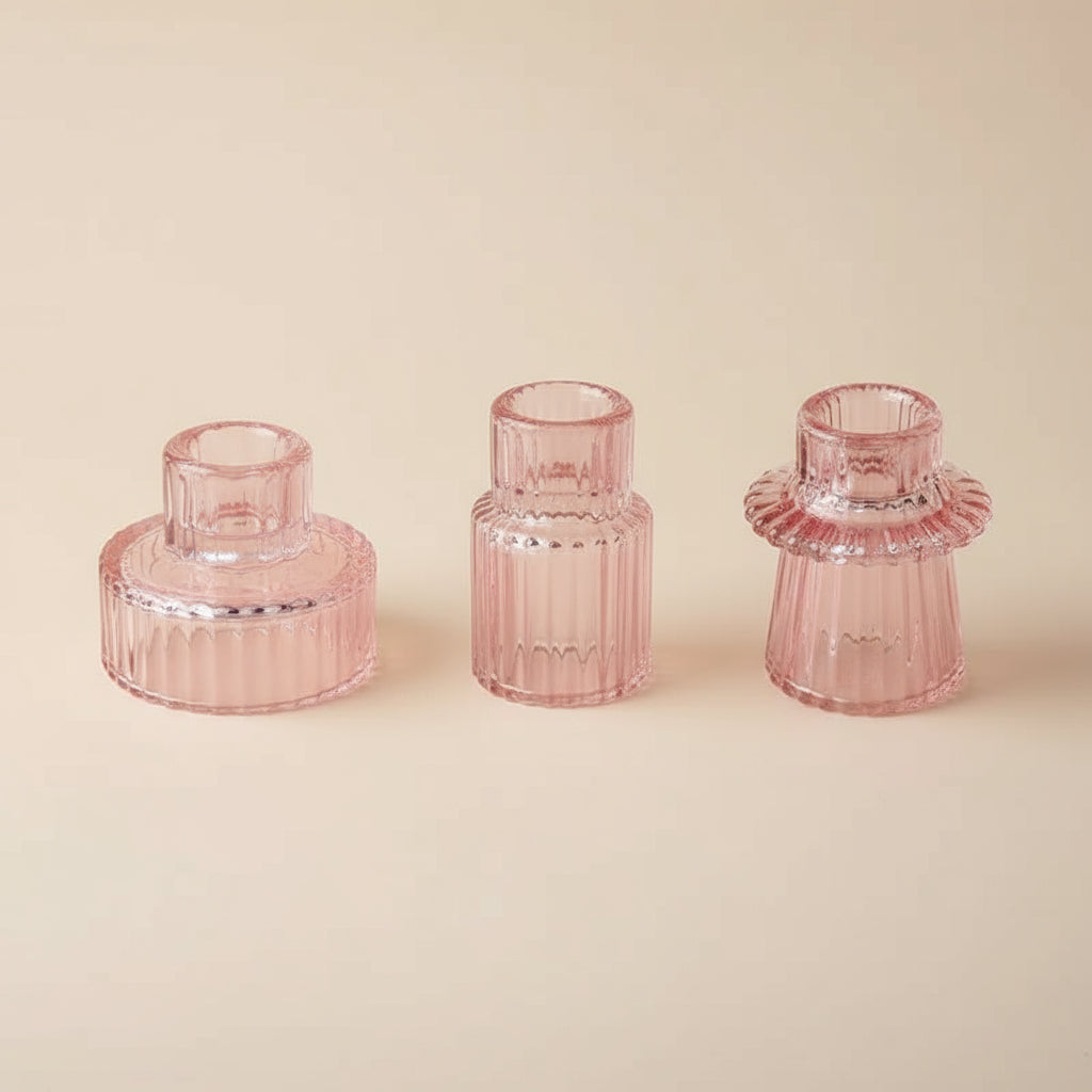 Three glass candlestick holders on a white surface. The holders have a textured, geometric, design in an pink colour.