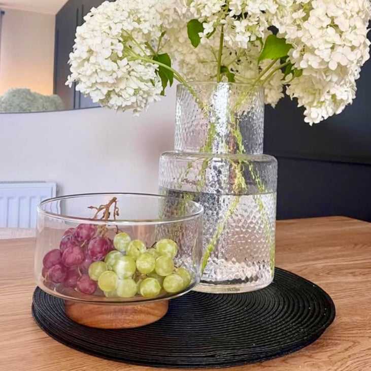 Clear vase with white flowers, glass bowl with grapes on a wooden table.