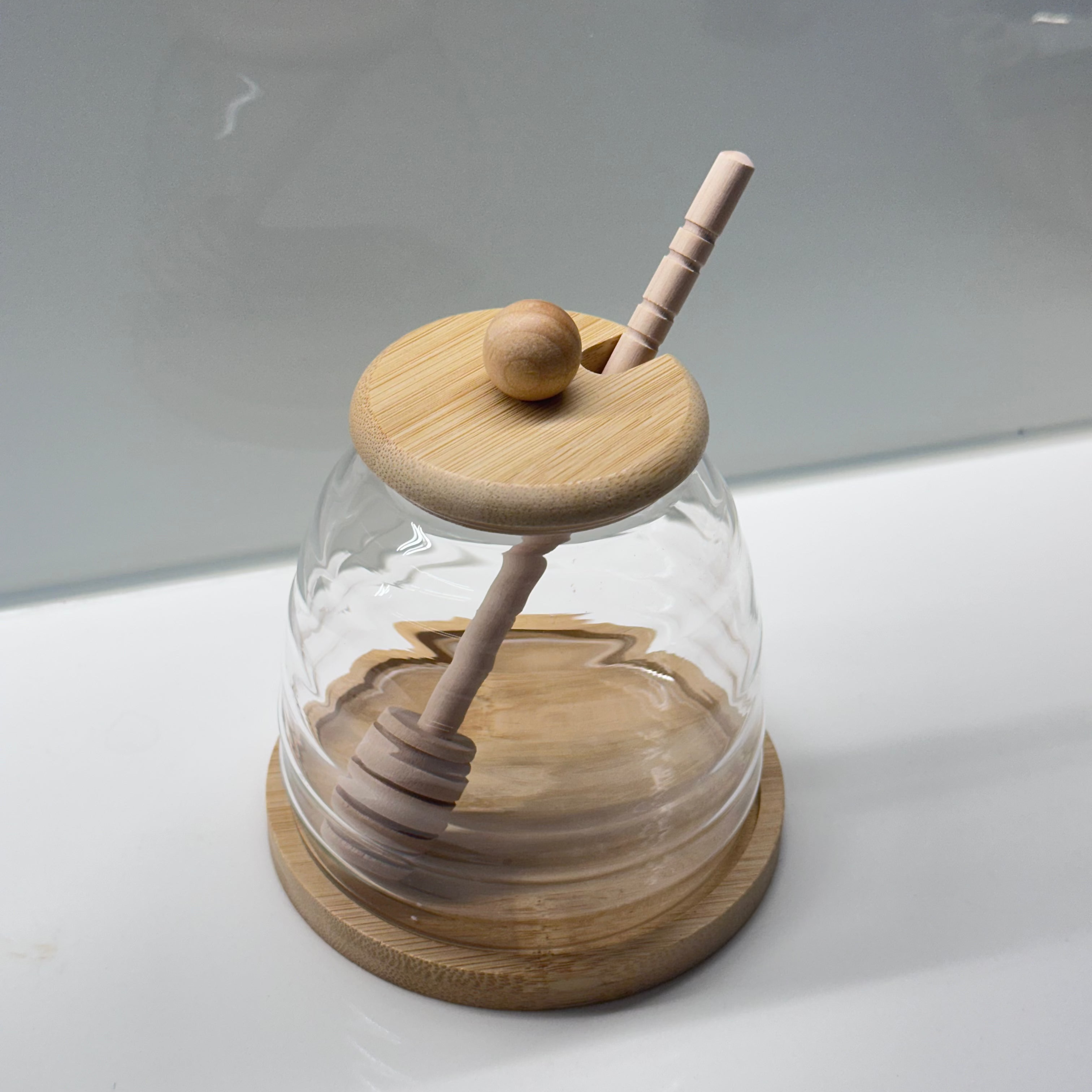 Wooden honey dipper inside a glass dome on a white surface with a gray background