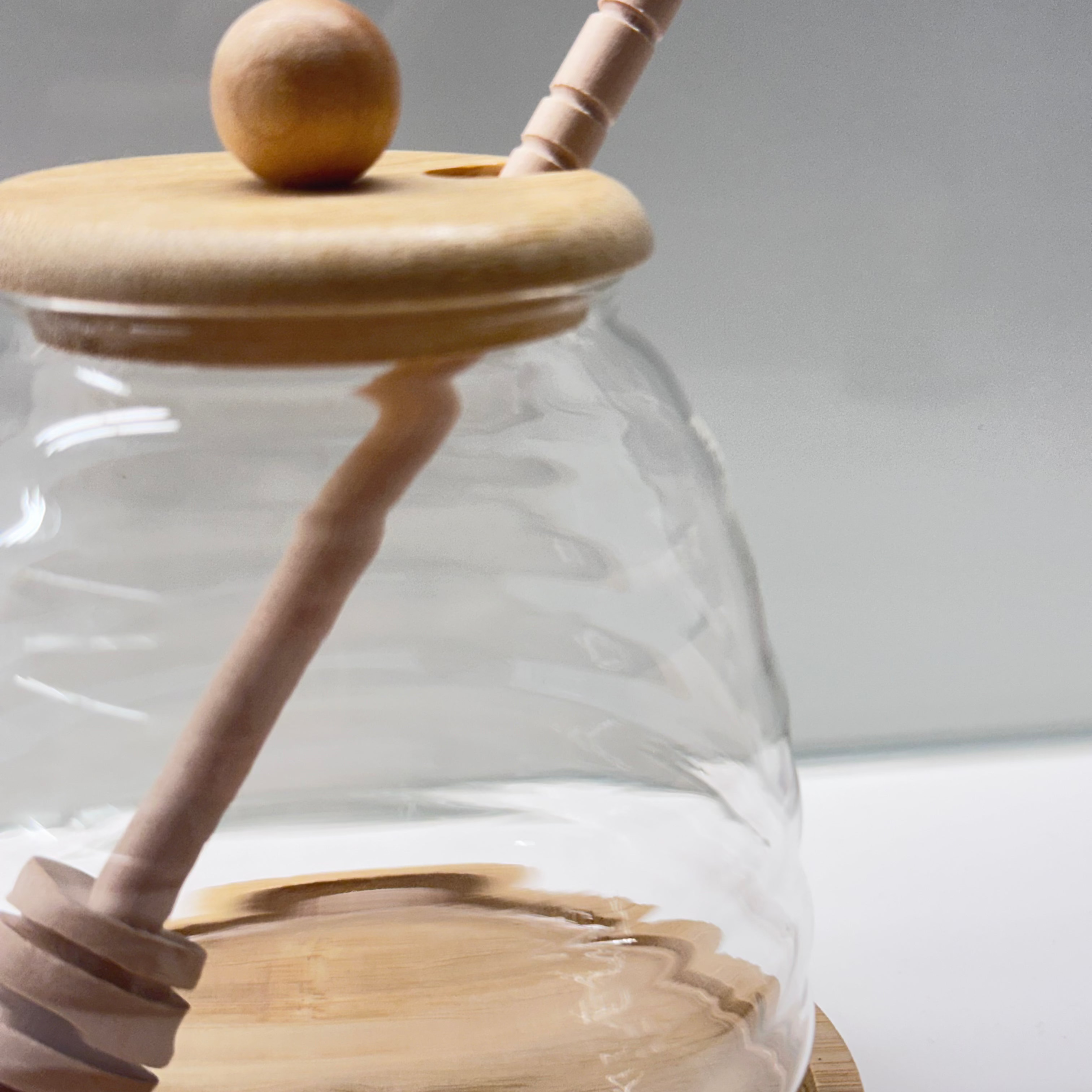 Glass jar with wooden lid and honey dipper on a white background