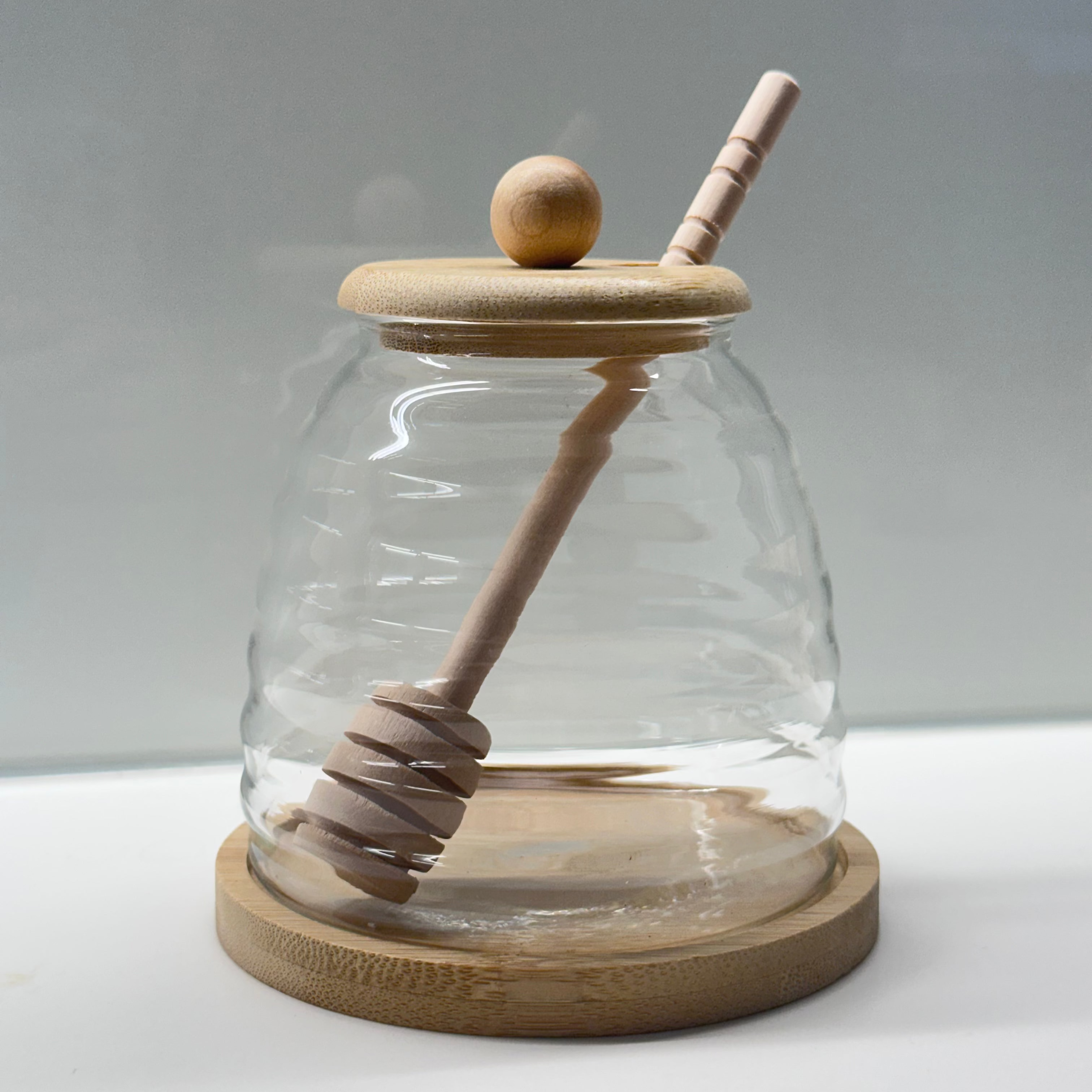 Glass honey jar with wooden lid and honey dipper on a white background