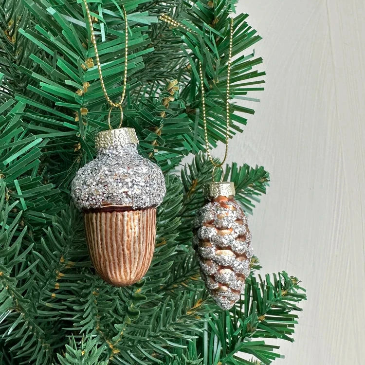 Glass pine cone and acorn ornaments with silver glitter. 4-piece set. Nature-inspired and elegant. Ideal for trees, wreaths, or festive accents. 