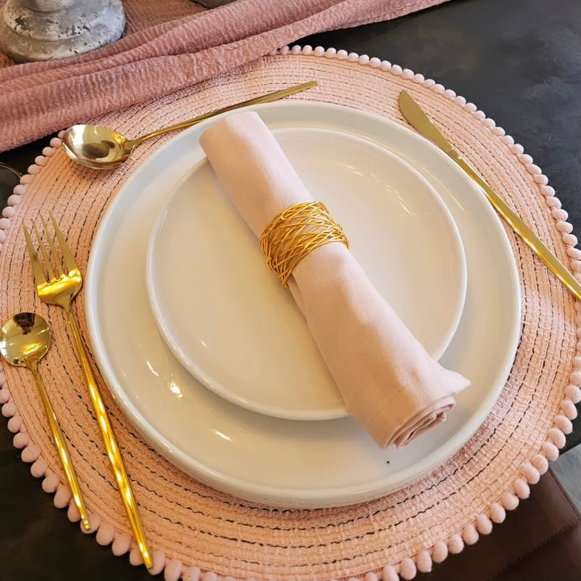 Elegant table setting with white plates, gold cutlery, and a pink napkin on a textured placemat.
