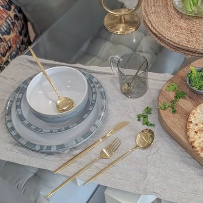 Dining table setting with gray plates, gold cutlery, and a glass on a light-colored tablecloth.