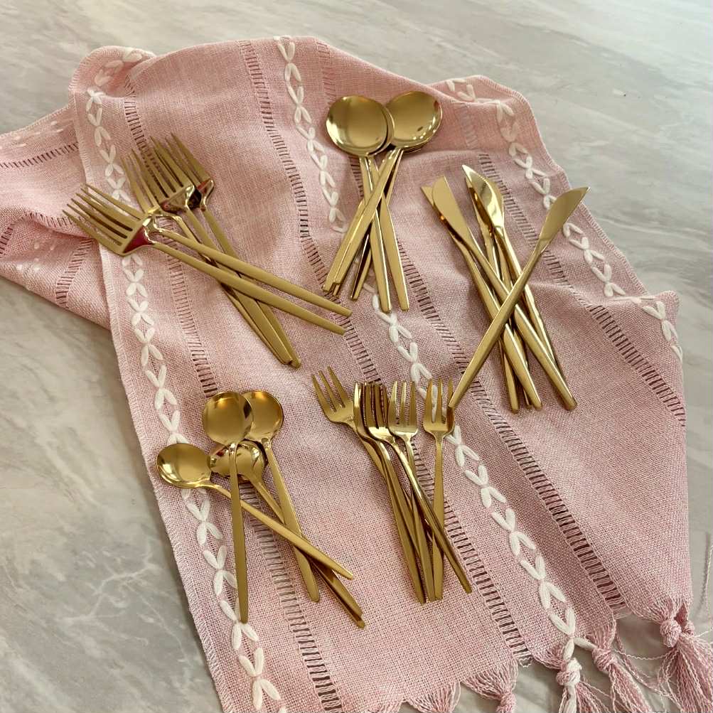 Set of gold cutlery on a pink table runner with white patterns