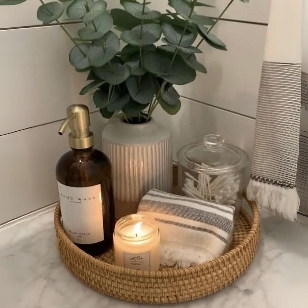 Handwoven, circular rattan tray in a bathroom setting. The tray contains soap, candle, and towel on a marble surface
