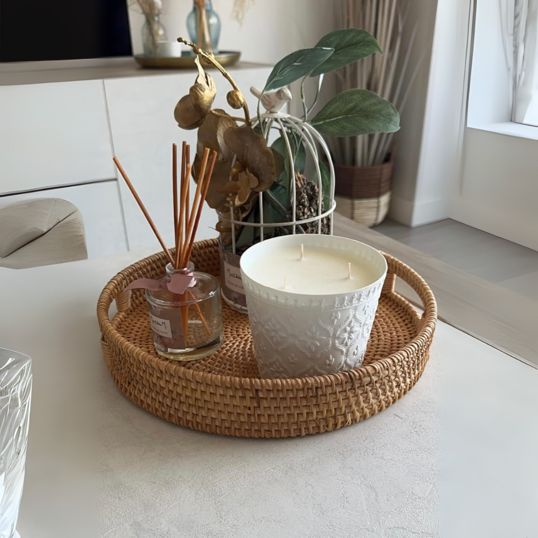 Handwoven, circular rattan tray with a candle, diffuser, and decorative items on a white surface.