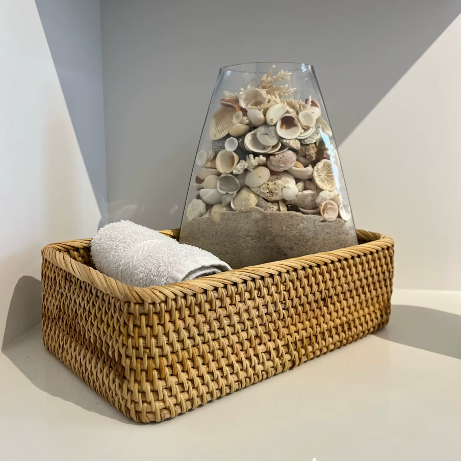 Woven basket with a glass container filled with seashells on a neutral background