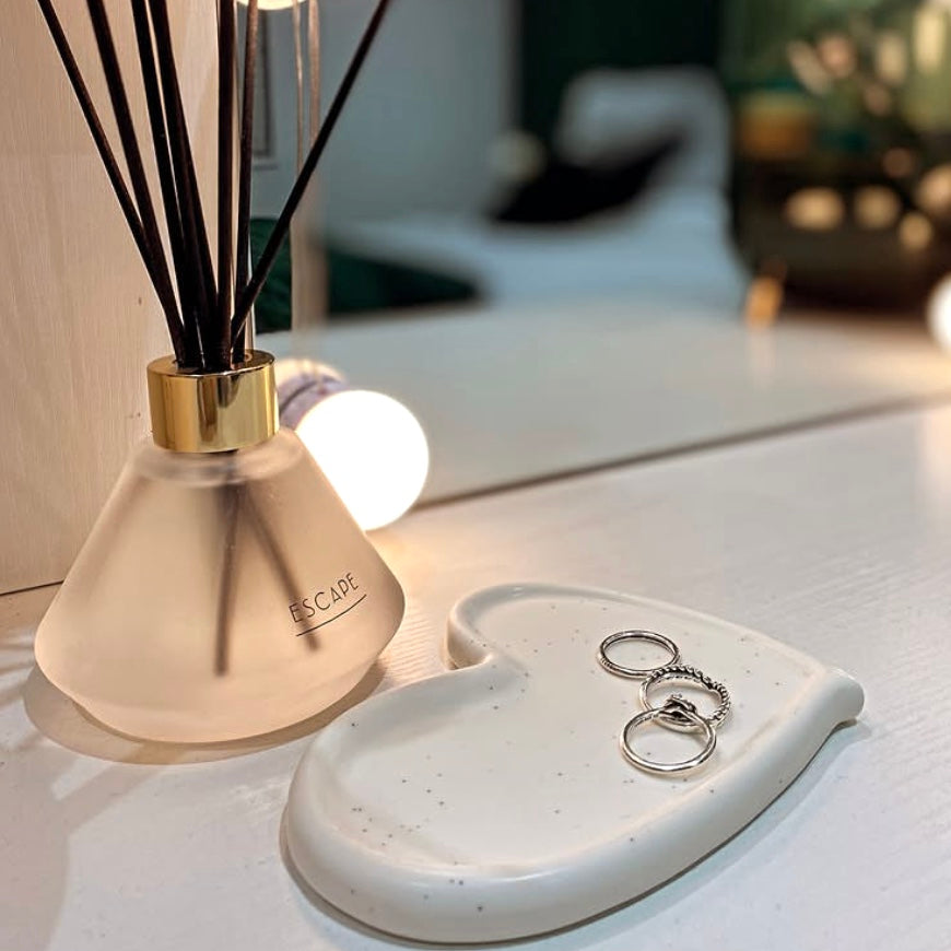 Diffuser with reeds and a heart-shaped dish with rings on a surface