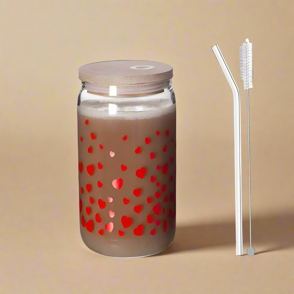 Drinking glass with small, red heart pattern, glass straw, and cleaning brush against a grey background