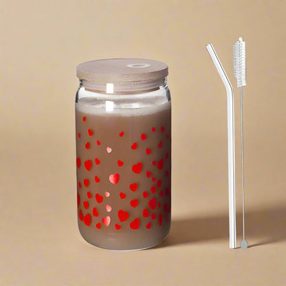 Drinking glass with small, red heart pattern, glass straw, and cleaning brush against a grey background