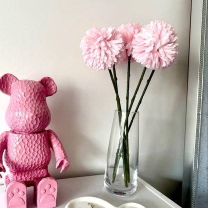 Pink teddy bear and vase with pink hydrangea flowers, and heart-shaped dish on a white surface.
