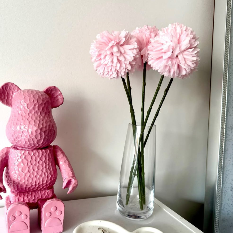 Pink teddy bear and vase with pink hydrangea flowers, and heart-shaped dish on a white surface.
