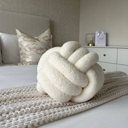 Decorative beige knot pillow on a bed in a bedroom setting