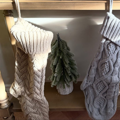 Two knitted stockings hanging on a hook with a small green tree between them.