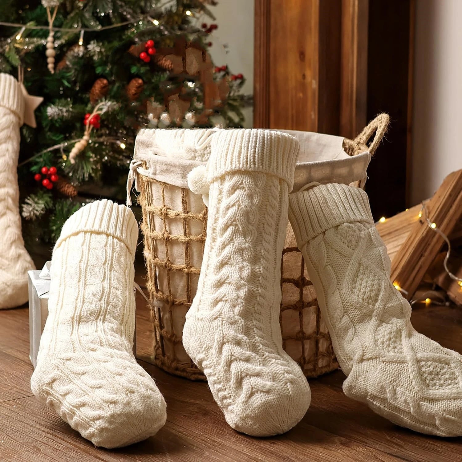 Three white cable-knitted Christmas stockings, each with a festive design and a Christmas tree in the background.