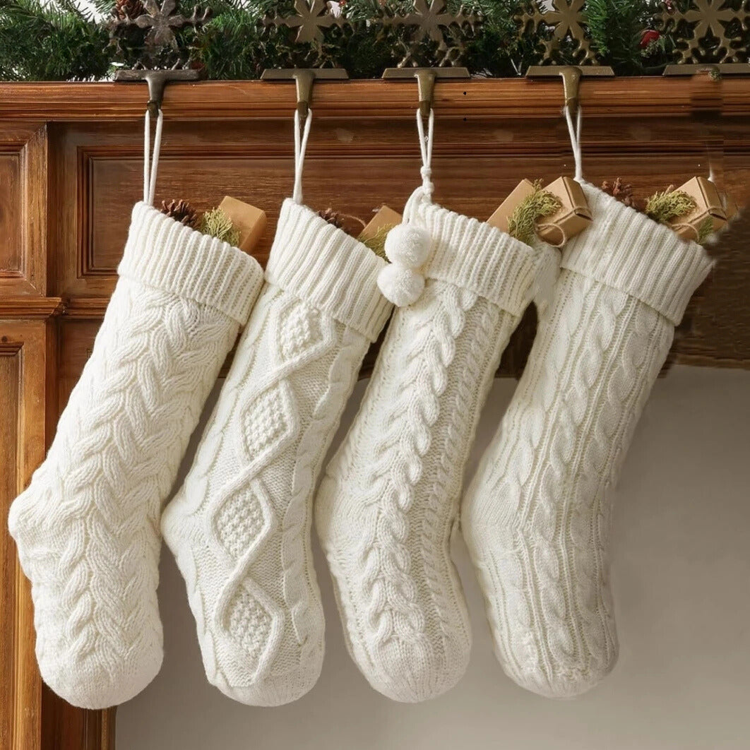 Four white cable-knitted Christmas stockings hanging from a wooden mantel, each with a festive design.
