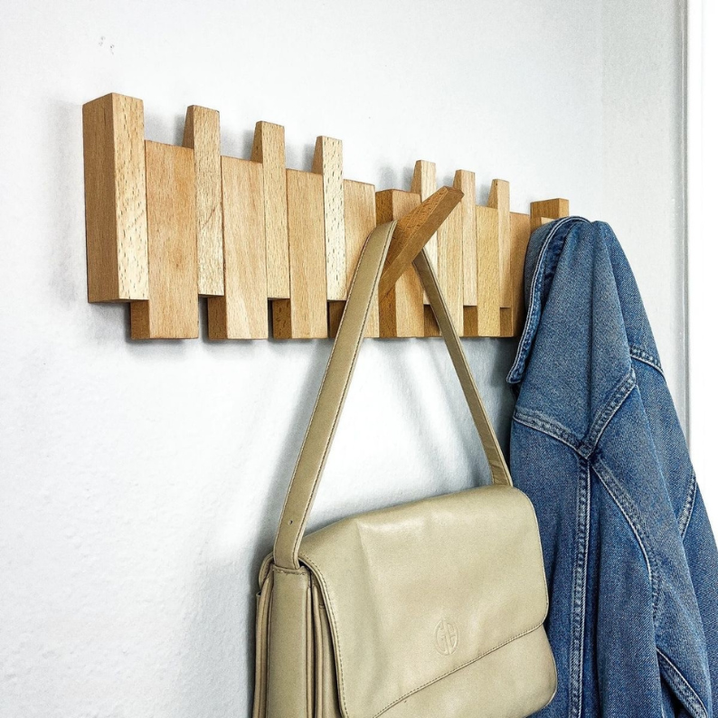 Wooden wall-mounted coat rack with a beige handbag and denim jacket on a white background