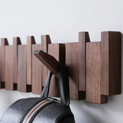 Wooden walnut coat rack on a white wall with a black bag hanging from one of them.
